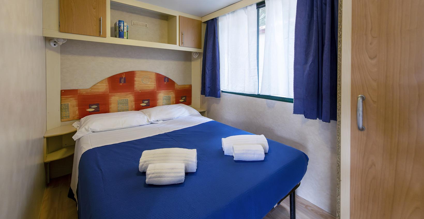Camera accogliente con letto matrimoniale, lenzuola blu e luce calda, atmosfera rilassante.