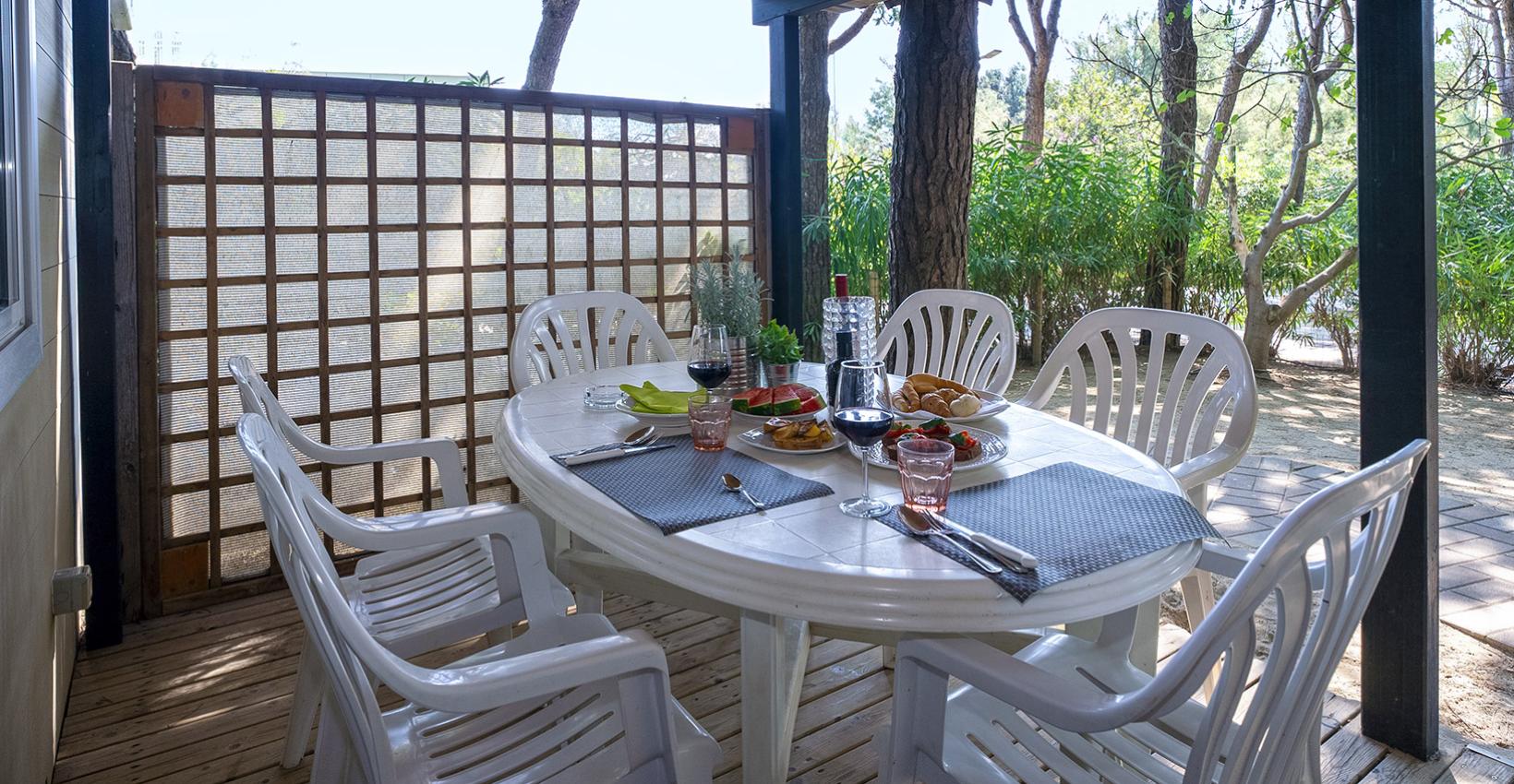 Veranda immersa nel verde, tavolo apparecchiato, atmosfera accogliente e rilassante per un pranzo all'aperto.