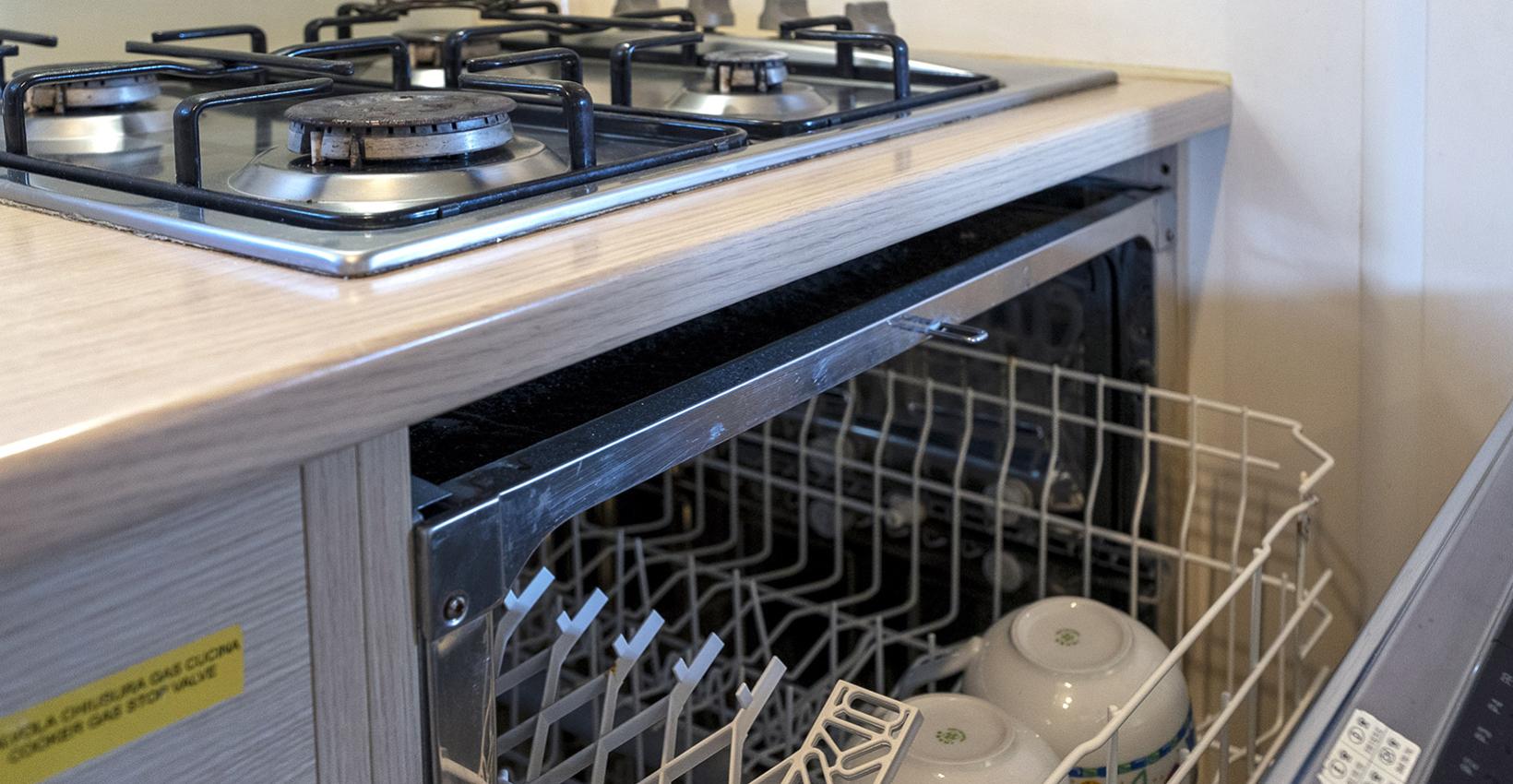 Cucina moderna con lavastoviglie aperta, stoviglie colorate, piano cottura a gas, atmosfera accogliente.