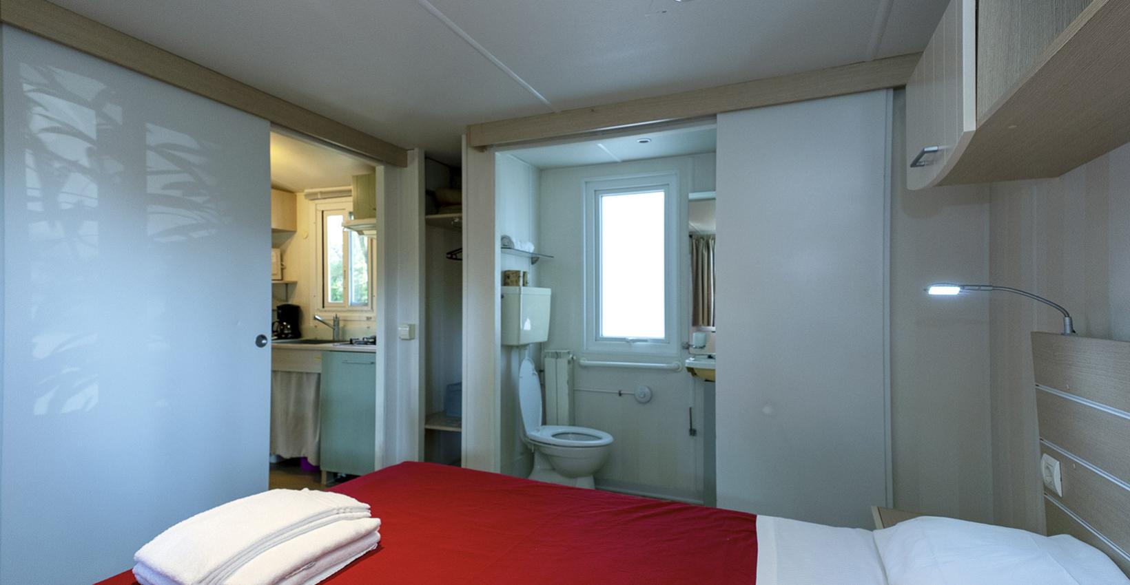 Camera accogliente con letto rosso, bagno privato e cucina, atmosfera calda e confortevole.