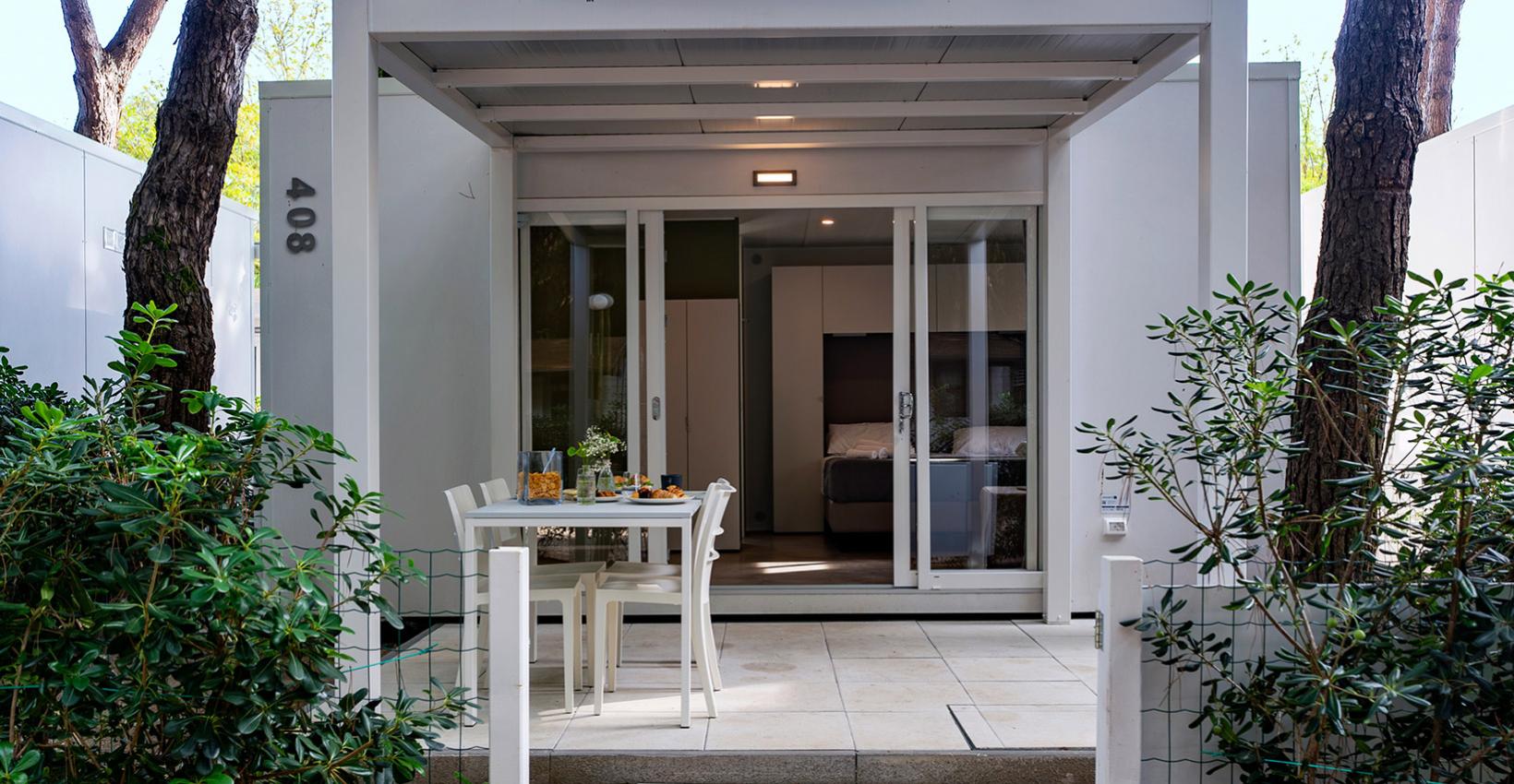 Piccolo bungalow moderno, immerso nella natura, con veranda accogliente e tavolo apparecchiato.