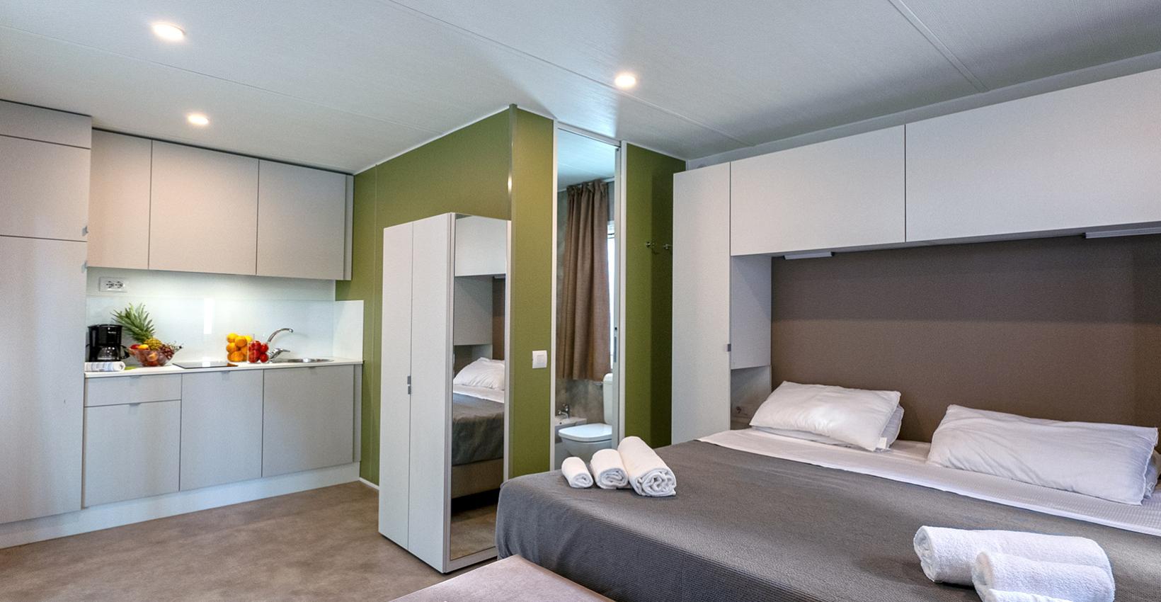 Moderno monolocale luminoso, letto accogliente, cucina compatta, giornali per relax, atmosfera serena.