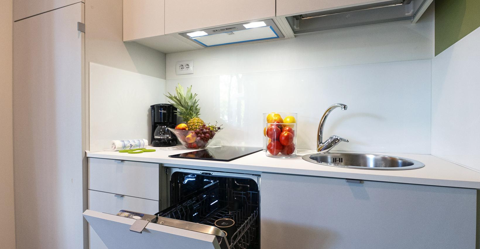 Cucina moderna, compatta, con frutta fresca, lavastoviglie aperta e luce calda.