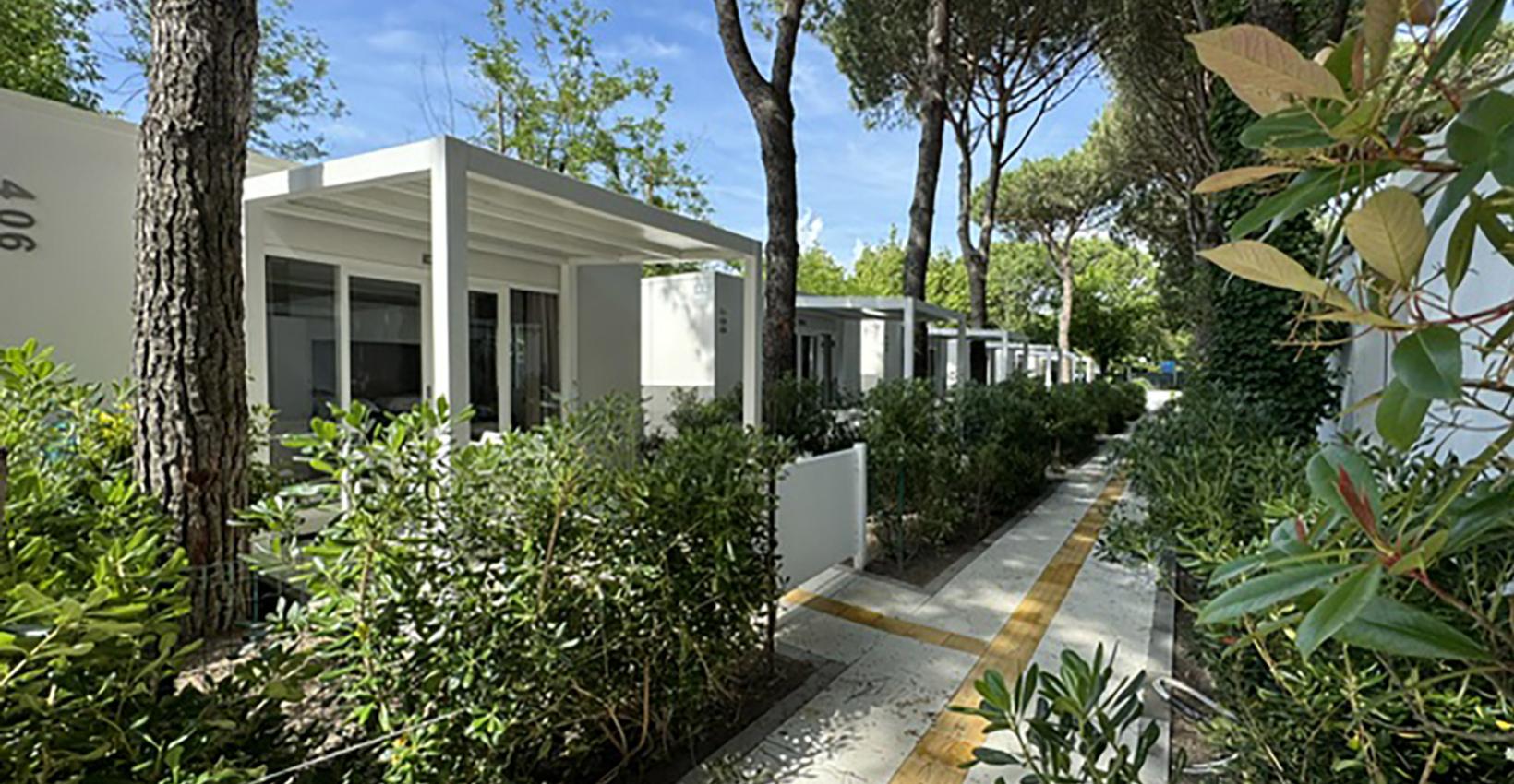 Bungalow moderni tra alberi e verde, atmosfera serena e naturale, cielo limpido.