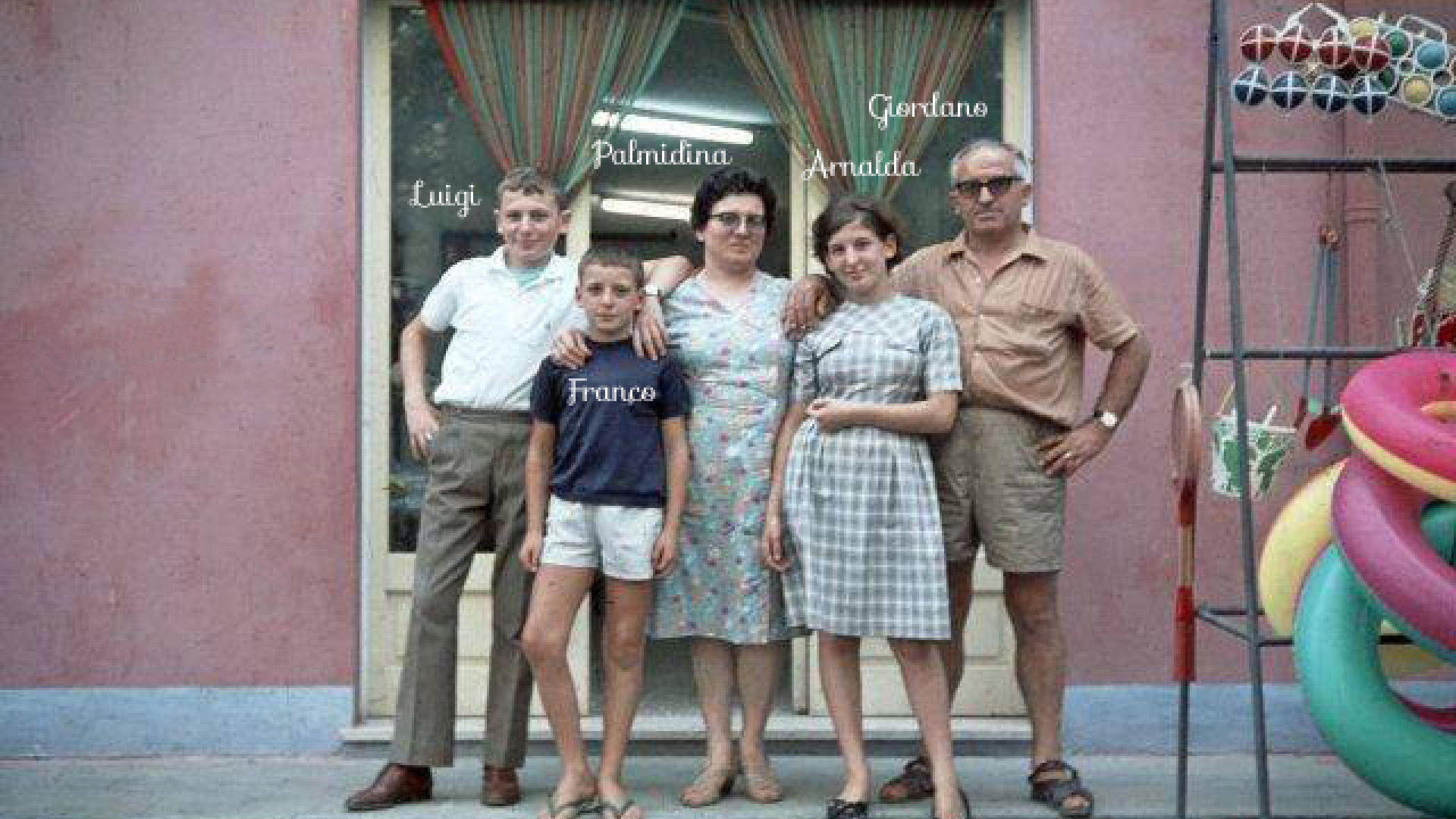 Famiglia unita e sorridente davanti a casa, con giochi colorati e atmosfera anni '60.