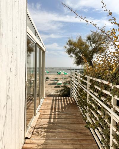 Passerella in legno, vista mare, ombrelloni verdi, atmosfera estiva e rilassante.