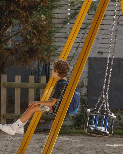 Bambino su altalena, sguardo lontano, atmosfera di riflessione e tranquillità nel parco giochi.