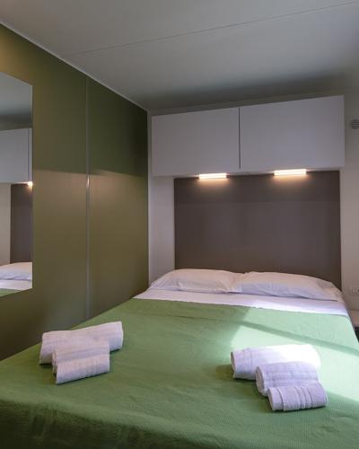 Camera accogliente con letto matrimoniale, lenzuola verdi, asciugamani bianchi e luce naturale.