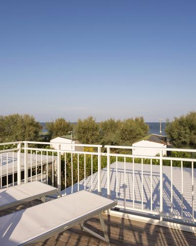 Terrazza soleggiata con sdraio, vista mare e alberi, atmosfera serena e rilassante.