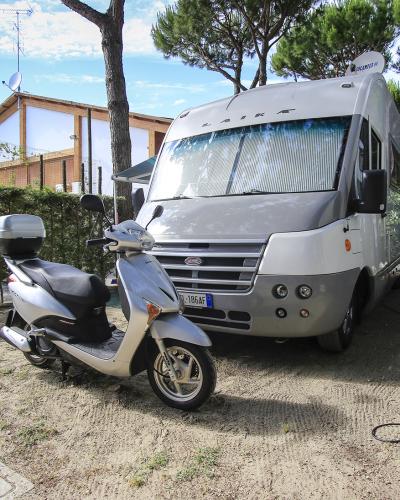Camper e scooter in campeggio tra alberi, atmosfera rilassante e avventurosa.