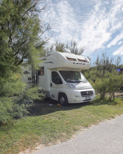 Camper immerso nella natura, sotto un cielo azzurro e nuvole soffici, atmosfera di libertà.