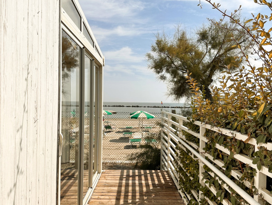 Passerella in legno, vista mare, ombrelloni verdi, atmosfera estiva e rilassante.