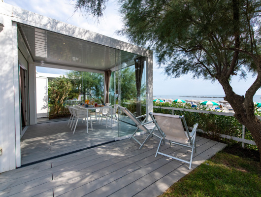Terrazza moderna vista mare, sedie bianche, ombrelloni colorati, atmosfera rilassante e naturale.