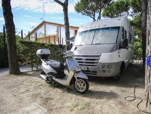 Camper e scooter in campeggio tra alberi, atmosfera rilassante e avventurosa.