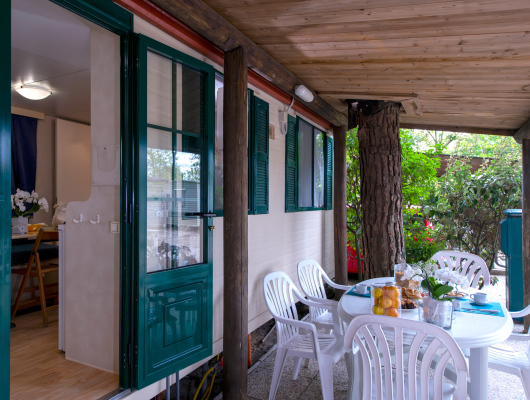 Veranda accogliente con tavolo imbandito, circondata da natura rigogliosa e atmosfera rilassante.