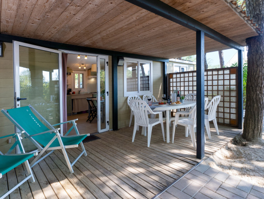 Veranda accogliente con tavolo apparecchiato, sedie bianche e sdraio verdi immerse nella natura.