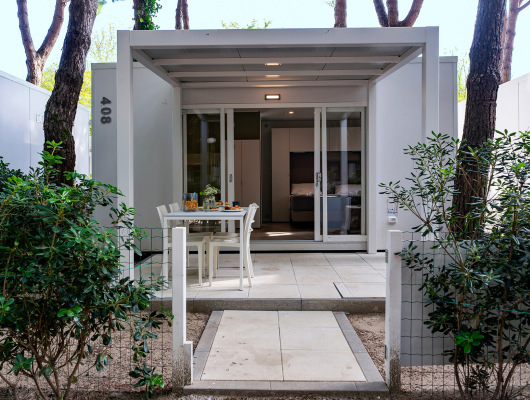 Piccolo bungalow moderno, immerso nella natura, con veranda accogliente e tavolo apparecchiato.