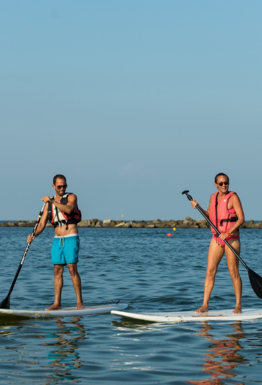 Due persone felici fanno paddleboarding in mare, guidate da un istruttore sotto il sole estivo.