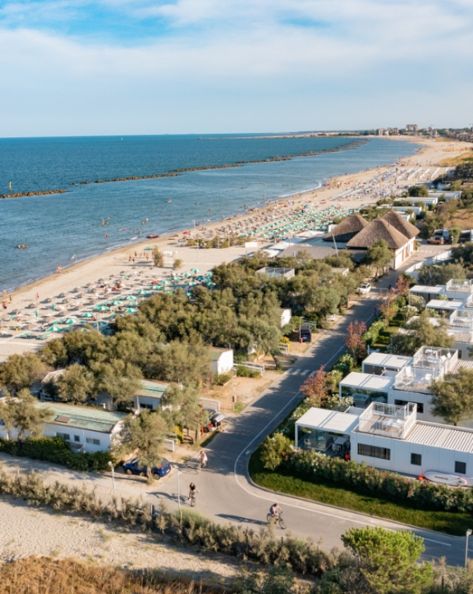Spiaggia soleggiata, mare calmo, ombrelloni colorati, villette moderne, atmosfera estiva rilassante e gioiosa.