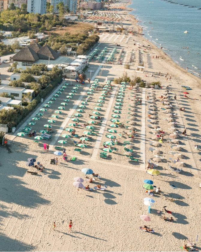 Spiaggia affollata, ombrelloni colorati, mare calmo, atmosfera estiva e vivace, relax e divertimento.