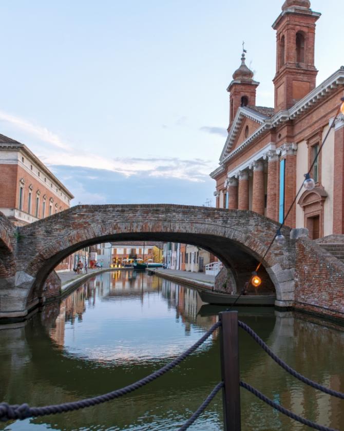 Ponte di mattoni riflesso su un canale, atmosfera serena al tramonto.