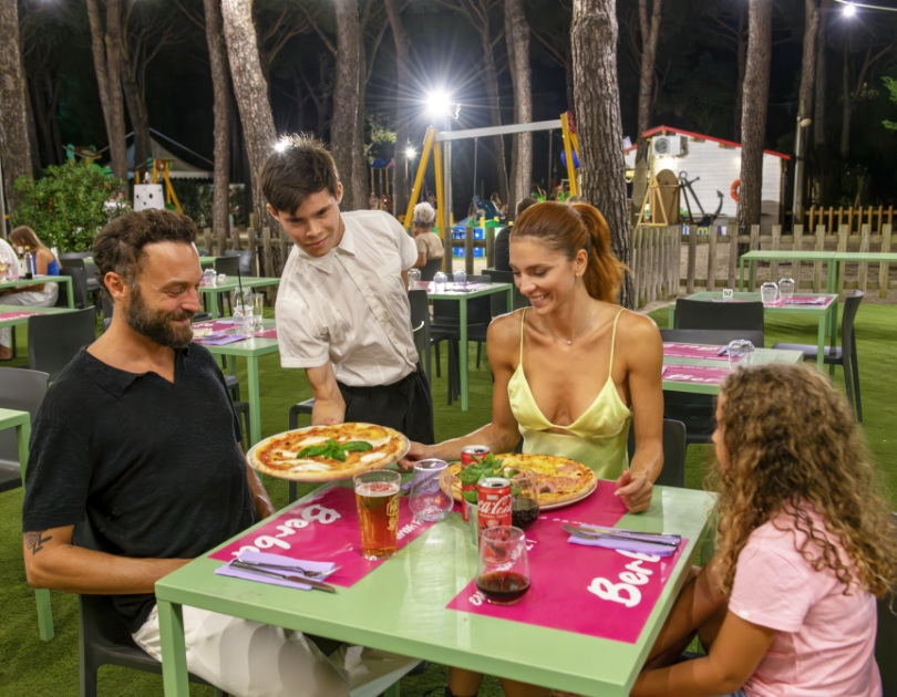 Famiglia felice cena all'aperto, pizze servite, atmosfera accogliente e serena tra alberi.