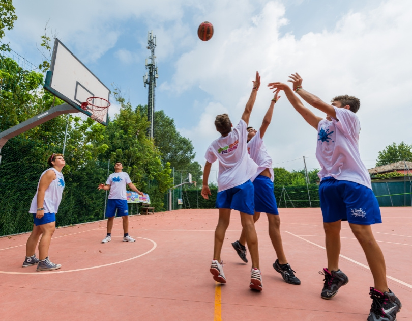 Giovani giocano a basket all'aperto, energia e competizione sotto un cielo azzurro.