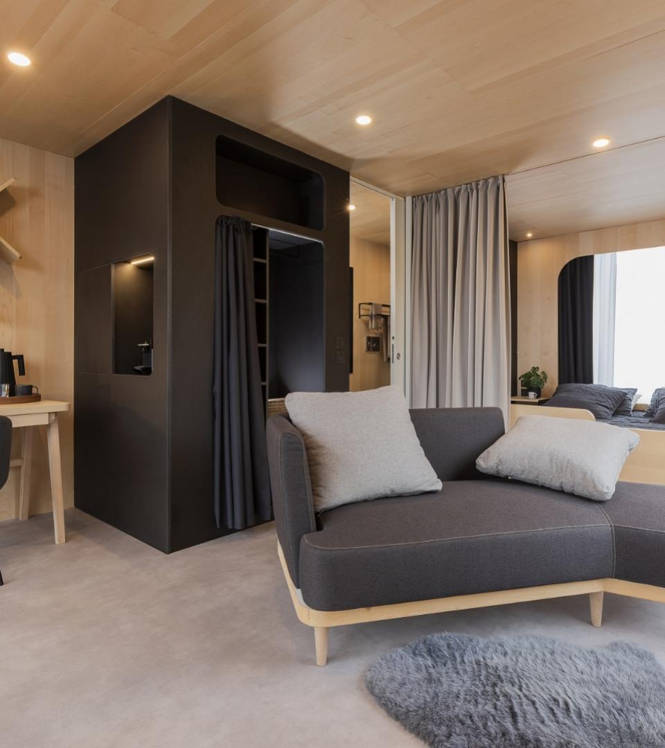 Interno moderno e accogliente, con divano grigio, legno chiaro e luci soffuse.